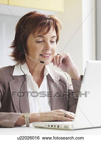 Stock Photograph - Senior woman with headset on laptop. Fotosearch