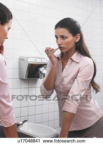 Woman reflected in office washroom mirror applying make-up View Large Photo Image Stock Image - Woman reflected in office washroom mirror applying make-up. Fotosearch
