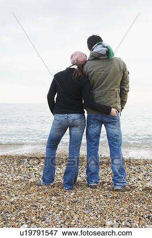 Stock Photo - Couple on beach, looking out to sea. Fotosearch