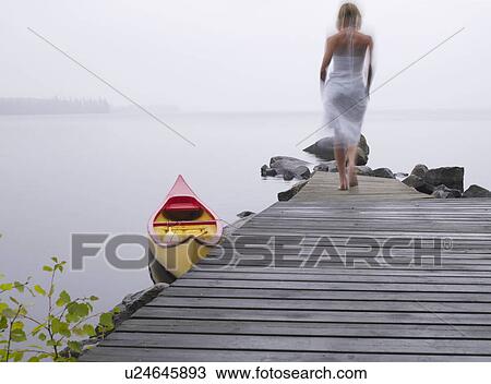 Stock Image - Woman walking on a dock near a boat.. Fotosearch