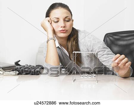Stock Photograph - Businesswomen sitting at her desk with a Newton's Cradle. Fotosearch