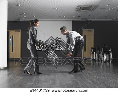Man and woman moving stack of chairs in empty presentation room View Large Photo Image Stock Photo - Man and woman moving stack of chairs in empty presentation room. Fotosearch