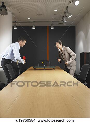 Picture - Man and woman playing miniature ping pong at boardroom table. Fotosearch