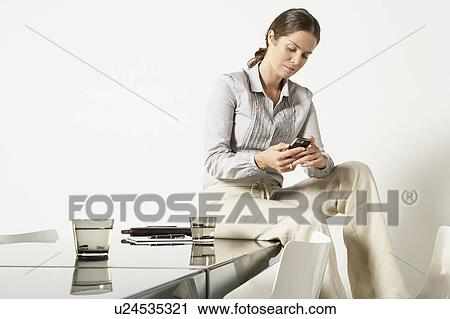 Young business woman seated on desk sending text message. View Large Photo Image Stock Image - Young business woman seated on desk sending text message.. Fotosearch