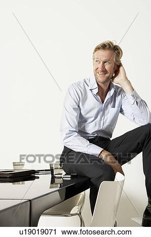 Young businessman seated on desk. View Large Photo Image Stock Image - Young businessman seated on desk.. Fotosearch