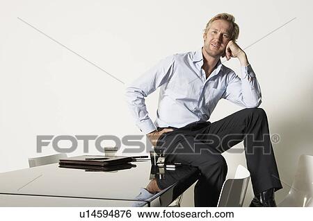 Stock Photograph - Young businessman seated on desk.. Fotosearch