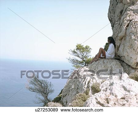 Stock Photo - Woman sitting on large rocks by the sea relaxing.. Fotosearch