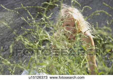 Stock Image - Young woman hiding behind bush.. Fotosearch