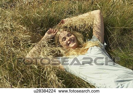 Picture - Young woman lying in long grass.. Fotosearch