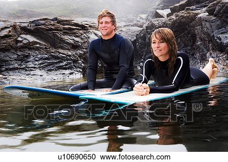 Couple lying on surfboards in the water smiling. View Large Photo Image Stock Image - Couple lying on surfboards in the water smiling.. Fotosearch
