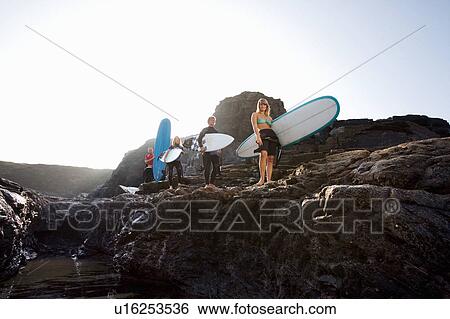 Four people carrying surfboards on large rocks smiling. View Large Photo Image Stock Photograph - Four people carrying surfboards on large rocks smiling.. Fotosearch