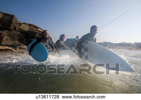 Four people running into the water with surfboards smiling. View Large Photo Image Stock Photo - Four people running into the water with surfboards smiling.. Fotosearch