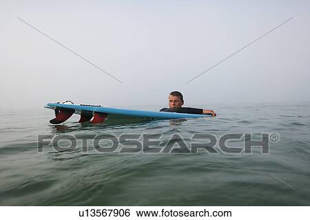 Man floating with surfboard in the water. View Large Photo Image Stock Photograph - Man floating with surfboard in the water.. Fotosearch