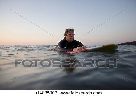 Stock Image - Man lying on surfboard in the water.. Fotosearch