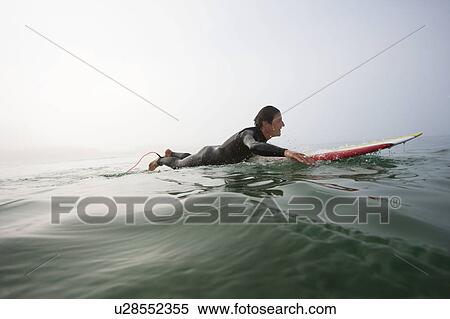Stock Photography - Man lying on surfboard in the water.. Fotosearch