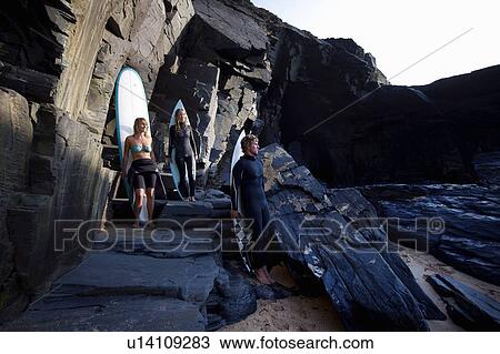 Three people standing with surfboards leaning on large rocks smiling. View Large Photo Image Stock Image - Three people standing with surfboards leaning on large rocks smiling.. Fotosearch