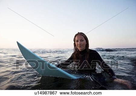 Stock Photo - Woman sitting on surfboard in the water.. Fotosearch