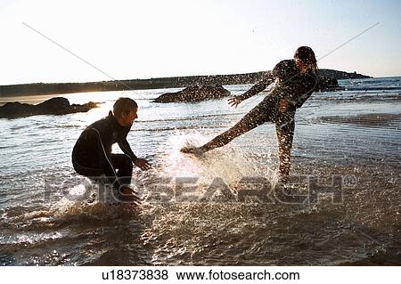 Couple in wetsuits splashing in shallow water. View Large Photo Image Stock Photo - Couple in wetsuits splashing in shallow water.. Fotosearch