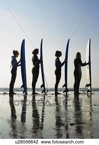 Stock Image - Four female surfers standing on a beach.. Fotosearch