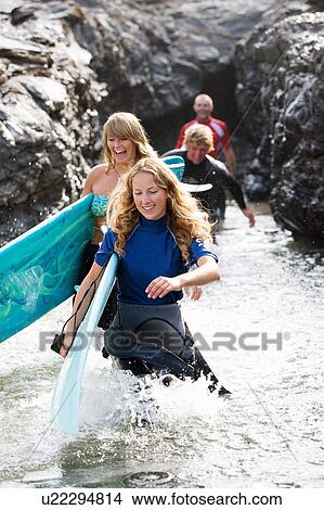 Four people carrying surfboards by large rocks smiling. View Large Photo Image Picture - Four people carrying surfboards by large rocks smiling.. Fotosearch