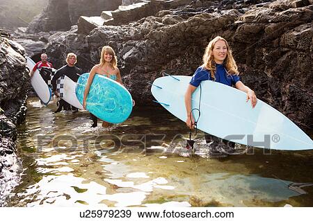 Four people carrying surfboards by large rocks smiling. View Large Photo Image Stock Photo - Four people carrying surfboards by large rocks smiling.. Fotosearch