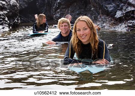 Stock Image - Four people lying on surfboards in the water smiling.. Fotosearch