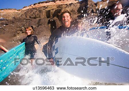 Four people running into the water with surfboards smiling. View Large Photo Image Stock Image - Four people running into the water with surfboards smiling.. Fotosearch