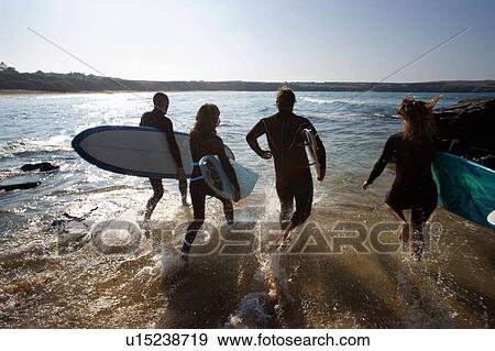 Four people running into the water with surfboards. View Large Photo Image Stock Photo - Four people running into the water with surfboards.. Fotosearch
