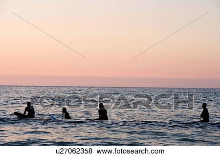 Stock Photo - Four people sitting on surfboards in the water.. Fotosearch