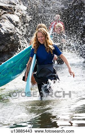 Four people splashing water carrying surfboards by large rocks smiling. View Large Photo Image Stock Image - Four people splashing water carrying surfboards by large rocks smiling.. Fotosearch