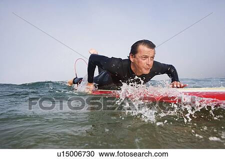 Stock Image - Man lying on surfboard in the water.. Fotosearch