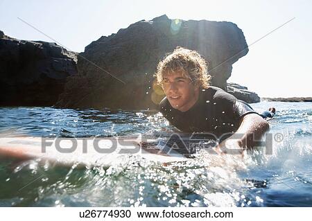 Stock Image - Man lying on surfboard in the water.. Fotosearch