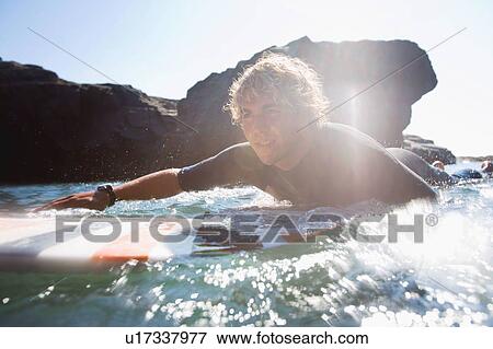 Man lying on surfboard in the water. View Large Photo Image Stock Photo - Man lying on surfboard in the water.. Fotosearch