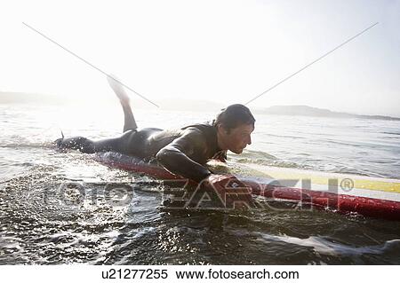 Man lying on surfboard in the water. View Large Photo Image Stock Photography - Man lying on surfboard in the water.. Fotosearch