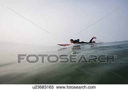 Stock Photography - Man lying on surfboard in the water.. Fotosearch