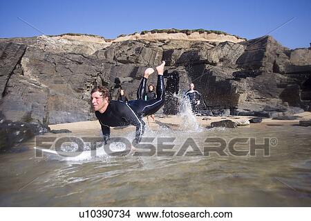 Picture - Man on surfboard with three surfers running into water behind him.. Fotosearch