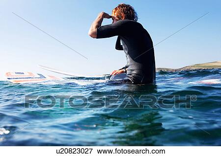 Stock Photo - Man sitting on surfboard in the water.. Fotosearch