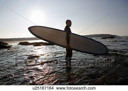 Man standing in shallow water with surfboard. View Large Photo Image Picture - Man standing in shallow water with surfboard.. Fotosearch