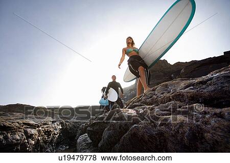 Three people carrying surfboards on large rocks smiling. View Large Photo Image Stock Photo - Three people carrying surfboards on large rocks smiling.. Fotosearch