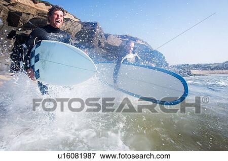 Two men running into the water with surfboards smiling. View Large Photo Image Stock Photo - Two men running into the water with surfboards smiling.. Fotosearch