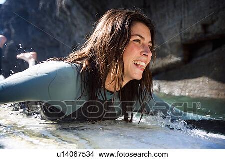 Woman lying on surfboard in the water smiling. View Large Photo Image Picture - Woman lying on surfboard in the water smiling.. Fotosearch