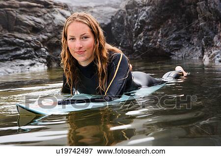 Stock Photo - Woman lying on surfboard in the water smiling.. Fotosearch