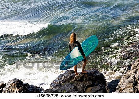 Woman standing with a surfboard on large rocks. View Large Photo Image Stock Photo - Woman standing with a surfboard on large rocks.. Fotosearch