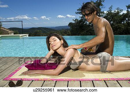 Stock Image - Couple sunbathing by a swimming pool. Fotosearch