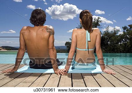 Couple sunbathing by a swimming pool View Large Photo Image Stock Image - Couple sunbathing by a swimming pool. Fotosearch
