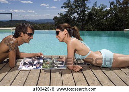 Couple sunbathing by a swimming pool with magazines View Large Photo Image Stock Photo - Couple sunbathing by a swimming pool with magazines. Fotosearch
