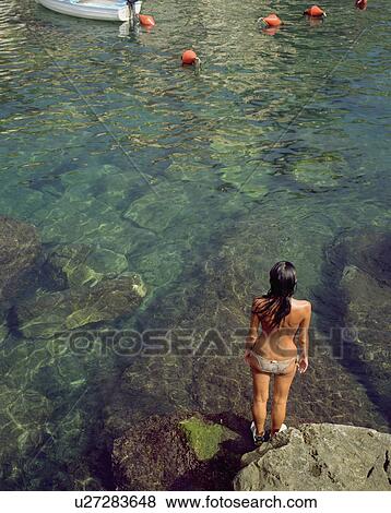Woman standing on a large rock by a boat in the water. View Large Photo Image Stock Photo - Woman standing on a large rock by a boat in the water.. Fotosearch