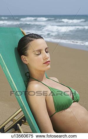 Young woman in bikini on beach lying in deck chair eyes closed sea in background. View Large Photo Image Stock Photography - Young woman in bikini on beach lying in deck chair eyes closed sea in background.. Fotosearch
