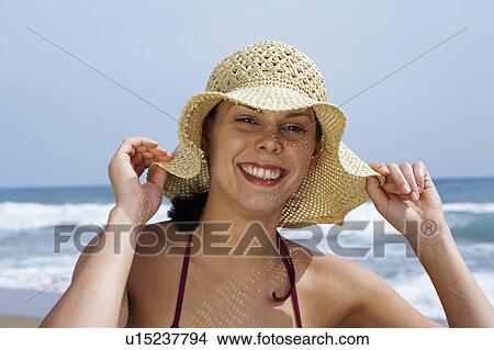 Young woman in bikini on beach with straw hat looking into camera sea in background. View Large Photo Image Picture - Young woman in bikini on beach with straw hat looking into camera sea in background.. Fotosearch