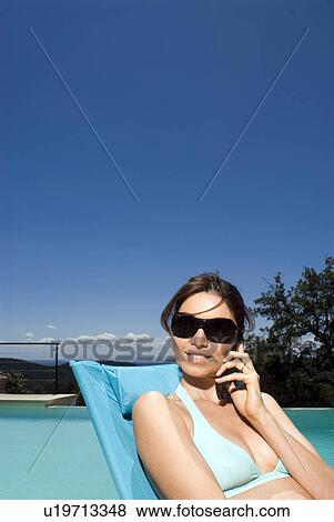 Stock Photo - Woman on cell phone by a swimming pool. Fotosearch